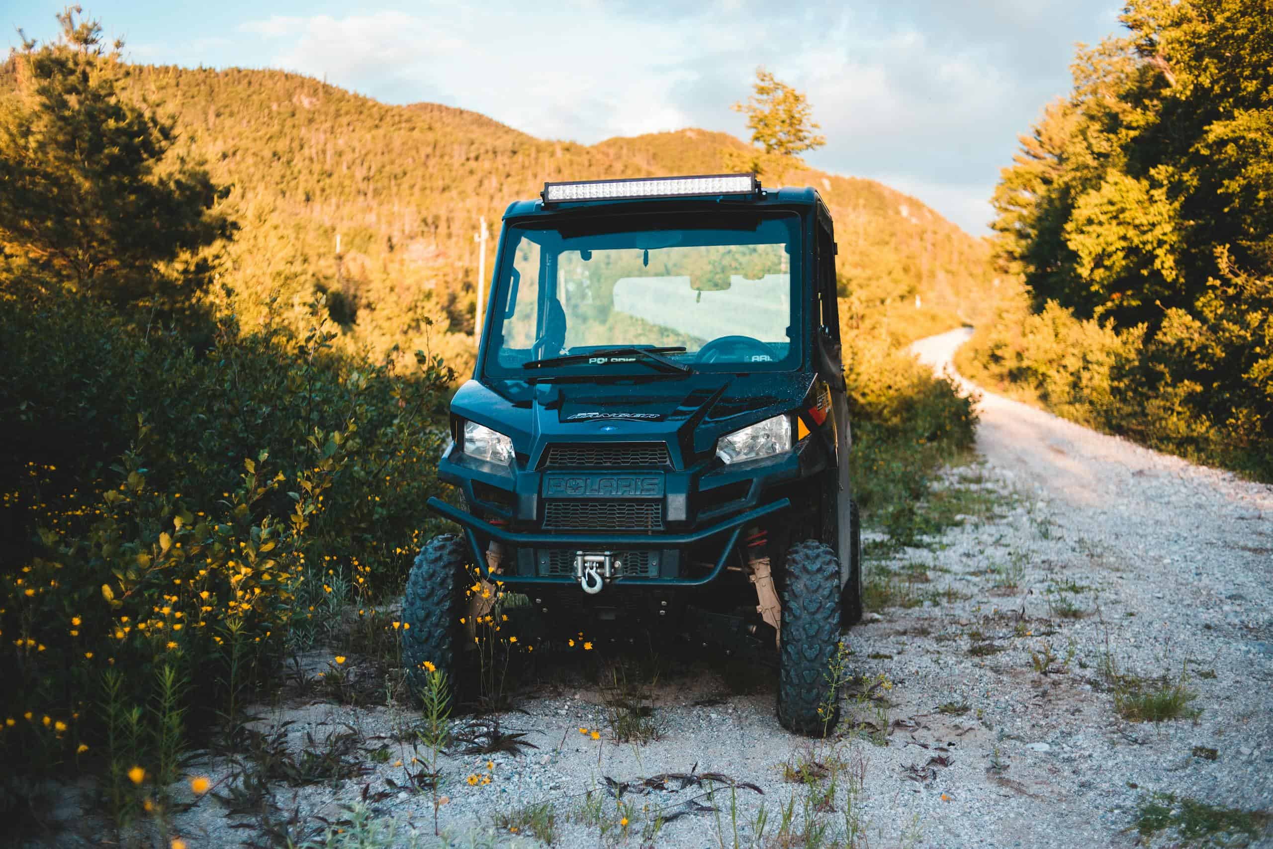 Aged all terrain vehicle near shabby pathway between bright trees growing on mount under cloudy sky